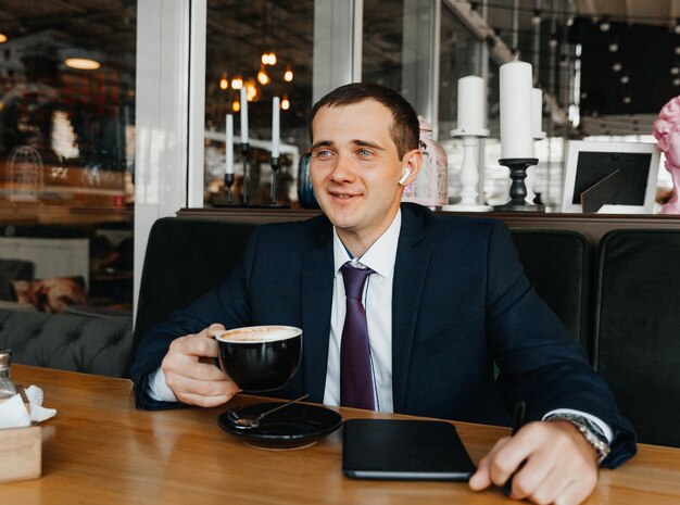 Hübscher junger Geschäftsmann lächelt und trinkt Kaffee in einem Café. Mann im Anzug mit Kaffee.