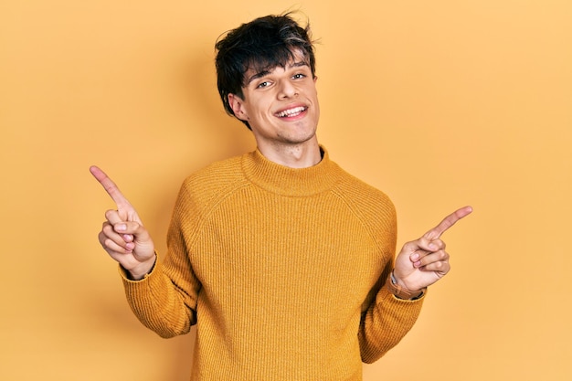 Hübscher junger Hipster-Mann in legerem gelben Pullover, der selbstbewusst lächelt und mit den Fingern in verschiedene Richtungen zeigt. Platz für Werbung kopieren