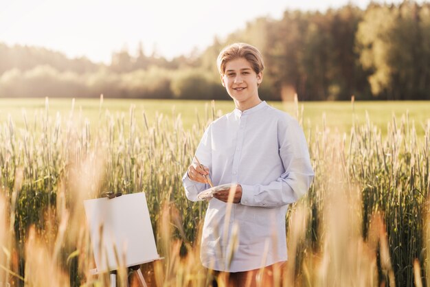 Hübscher junger Künstler mit Staffelei in der Natur im Sommer. kreatives Hobby