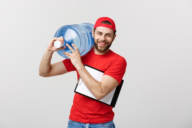 Hübscher junger Lieferarbeiter in der roten Uniform hält eine Flasche Wasser