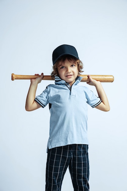 Hübscher junger lockiger Junge in Freizeitkleidung auf weißer Wand. Selbstbewusst und cool mit Sportschläger. Kaukasischer männlicher Vorschulkind mit hellen Gesichtsgefühlen. Kindheit, Ausdruck, Spaß haben.