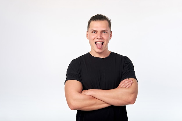 Hübscher junger lustiger Mann, der ein schwarzes Baumwoll-T-Shirt trägt, das Zunge zeigt