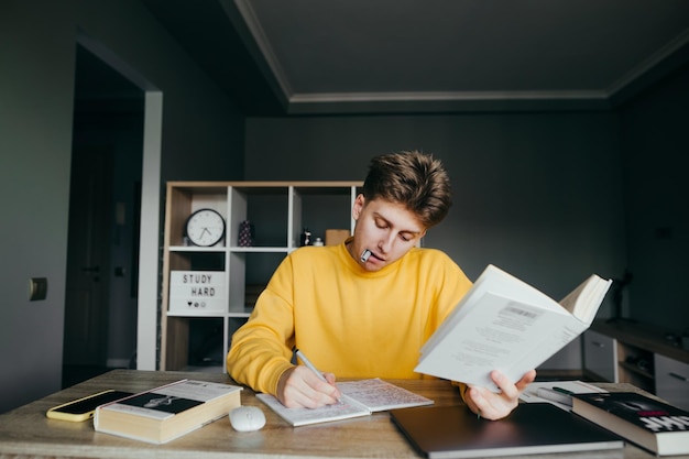 Hübscher junger männlicher Student in gelber Freizeitkleidung studiert zu Hause an einem Tisch