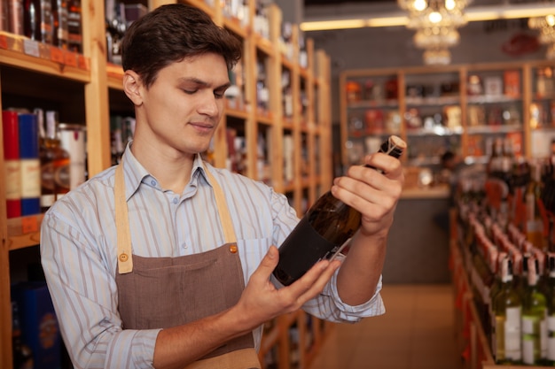 Hübscher junger männlicher Winzer, der Schürze trägt, Flasche Wein hält, Kopienraum