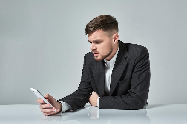 Hübscher junger Mann, der am Handy spricht, während er an seinem Arbeitsplatz im Büro sitzt