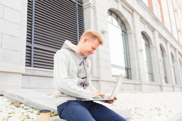 Hübscher junger Mann, der am Laptop arbeitet und auf der Stadtstraße lächelt