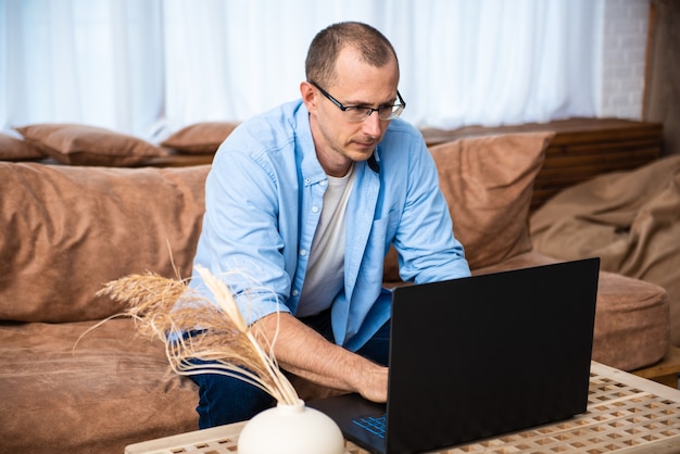 Hübscher junger Mann, der auf der Couch sitzt und am Laptop arbeitet