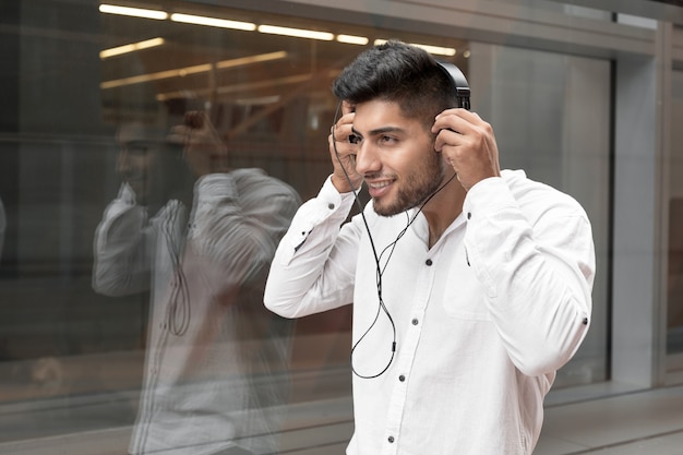 Hübscher junger Mann, der auf der Straße lächelt und Musik hört