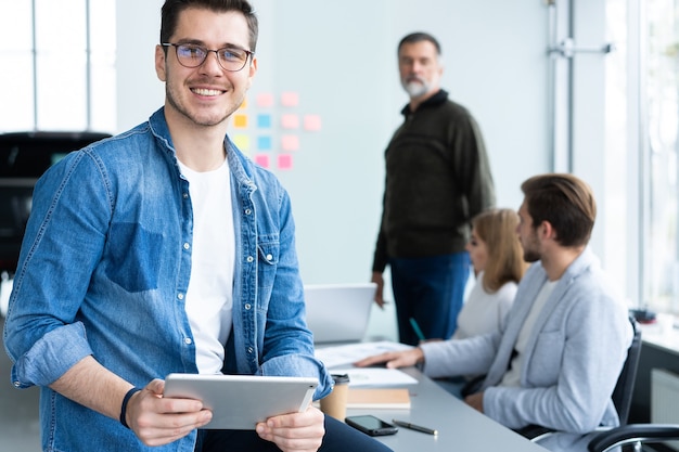 Hübscher junger Mann, der digitales Tablett hält und im Büro lächelt