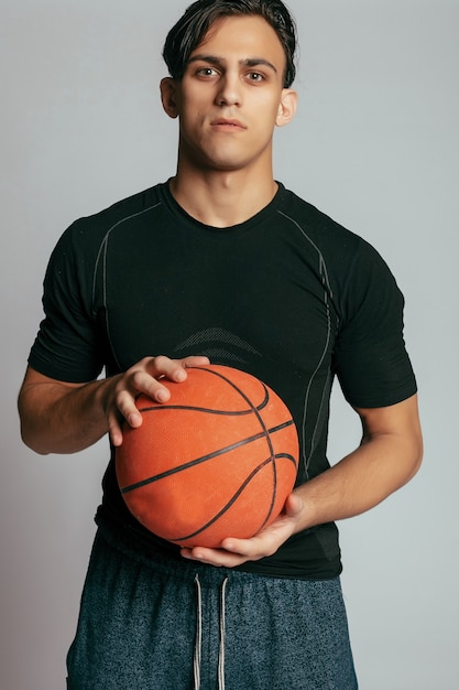 Hübscher junger Mann, der einen Basketballball trägt