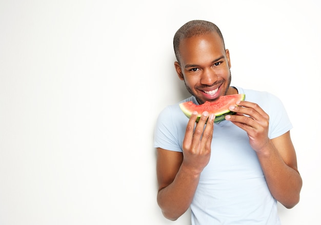 Hübscher junger Mann, der frische Wassermelone lächelt und isst