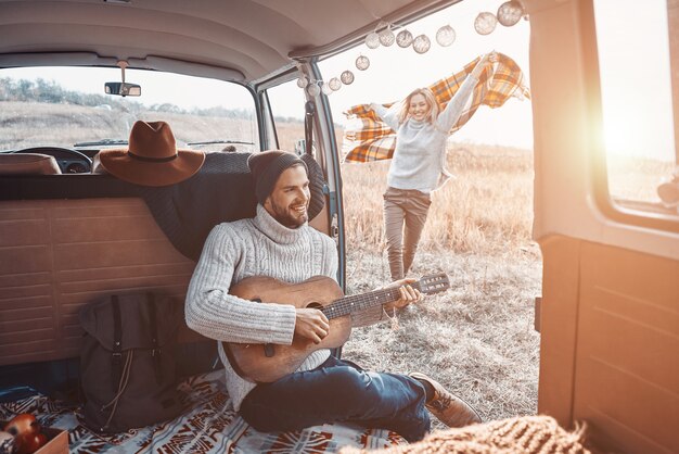 Hübscher junger Mann, der Gitarre für seine Freundin spielt, während er Zeit im Wohnmobil verbringt