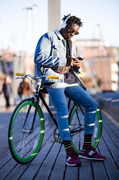 Hübscher junger Mann, der Handy und örtlich festgelegtes Gangfahrrad in der Straße verwendet.