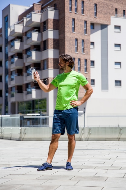 Hübscher junger Mann, der Handy während der Übung verwendet