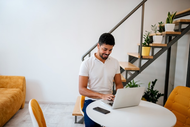 Hübscher junger Mann, der Laptop am modernen gemütlichen Haus verwendet.