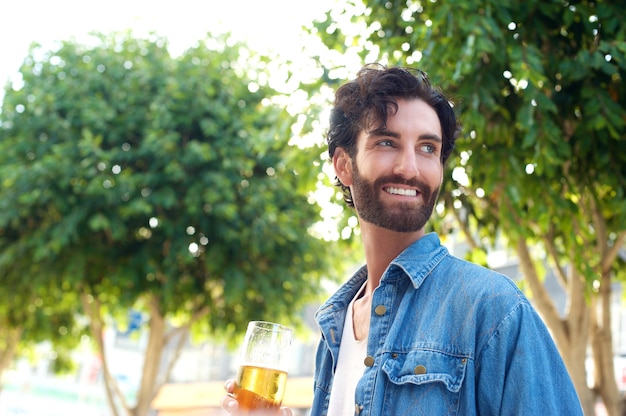 Hübscher junger Mann, der mit Glas Bier lächelt