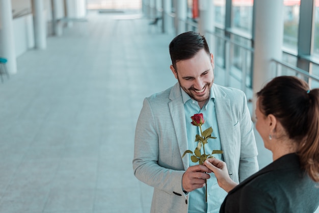 Hübscher junger Mann, der seiner Freundin eine Rose gibt. Überraschungsbesuch bei der Arbeit.