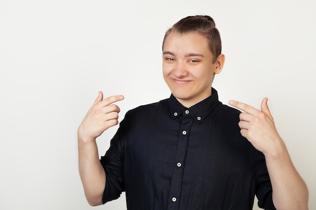 Hübscher junger Mann, der selbstbewusst lächelnd zeigt und Finger auf seinen Mund mit einem Lächeln auf seinem Gesicht zeigt. Ein Student mit einem selbstbewussten Gesichtsausdruck zeigt mit den Fingern auf ein Lächeln.