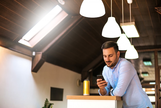 Hübscher junger Mann, der Smartphone in der Küche steht und verwendet.