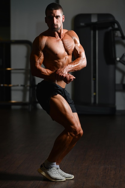 Hübscher junger Mann, der stark in der Turnhalle steht und Muskeln muskulöser athletischer Bodybuilder-Eignungs-Modell aufwirft, das nach Übungen aufwirft