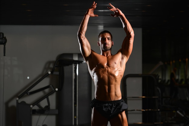 Hübscher junger Mann, der stark in der Turnhalle steht und Muskeln muskulöser athletischer Bodybuilder-Eignungs-Modell aufwirft, das nach Übungen aufwirft