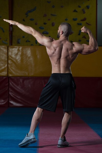 Hübscher junger Mann, der stark in der Turnhalle steht und Muskeln muskulöser athletischer Bodybuilder-Eignungs-Modell aufwirft, das nach Übungen aufwirft