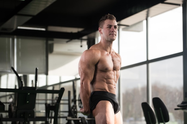 Hübscher junger Mann, der stark in der Turnhalle steht und Muskeln muskulöser athletischer Bodybuilder-Eignungs-Modell aufwirft, das nach Übungen aufwirft