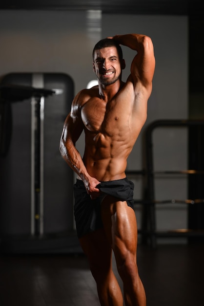 Hübscher junger Mann, der stark in der Turnhalle steht und Muskeln muskulöser athletischer Bodybuilder-Eignungs-Modell aufwirft, das nach Übungen aufwirft