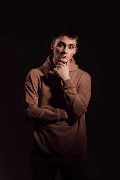 Hübscher junger Mann im braunen Pullover steht vor dunklem Hintergrund