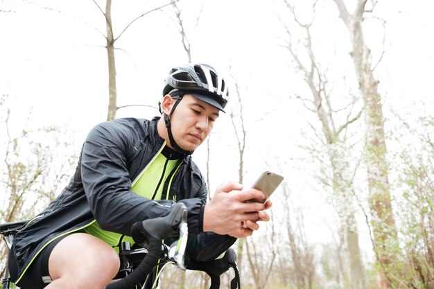 Hübscher junger Mann im Fahrradhelm mit Fahrrad mit Smartphone im Park