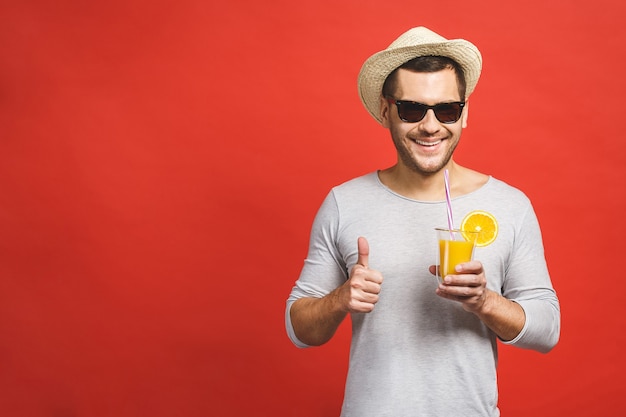 Hübscher junger Mann im Hut und in der Sonnenbrille, die frischen Orangensaft trinken