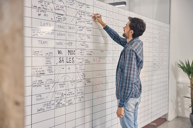 Hübscher junger Mann im karierten Hemd, der die Planertafel bei der Arbeit ausfüllt