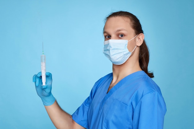 Hübscher junger Mann in Arztuniform mit Spritze auf blauem Hintergrund