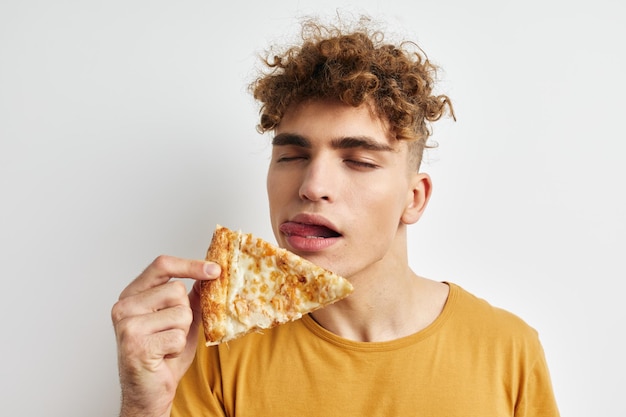 Hübscher junger Mann in einem gelben T-Shirt, der Pizza isst Lifestyle unverändert