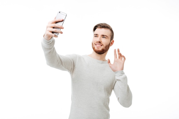 Hübscher junger Mann in einem weißen Pullover, der das Telefon benutzt