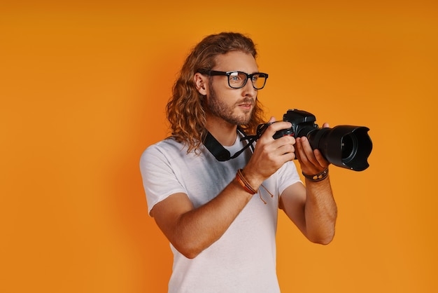 Hübscher junger Mann in Freizeitkleidung mit Fotokamera beim Stehen gegen gelbe Wand