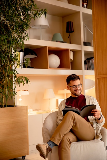 Hübscher junger Mann in Freizeitkleidung und mit Brille, die ein Buch zu Hause liest