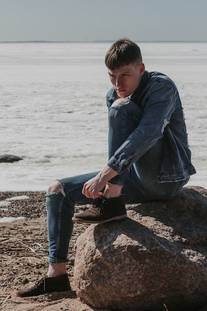 Hübscher junger Mann in zerrissenen Jeans, der an etwas am Winterstrand denkt.