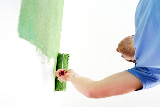 hübscher junger mann malt in blauer und grüner farbe weiße wand des neuen hauses