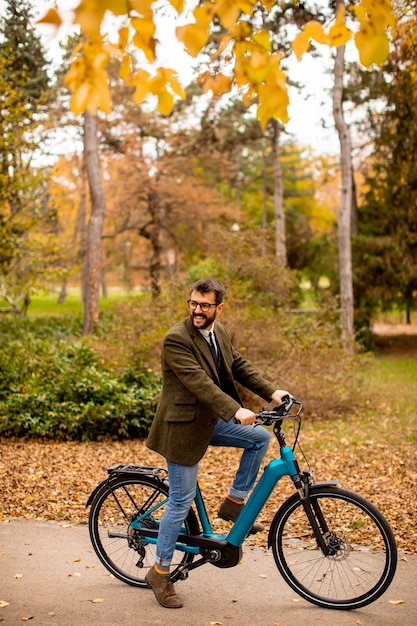 Hübscher junger Mann mit Elektrofahrrad im Herbstpark