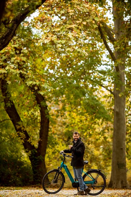 Hübscher junger Mann mit Elektrofahrrad im Herbstpark