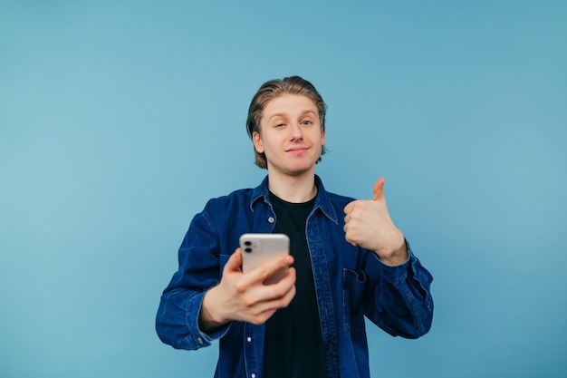 hübscher junger mann mit langer taille und in einem blauen hemd steht mit einem smartphone in der hand