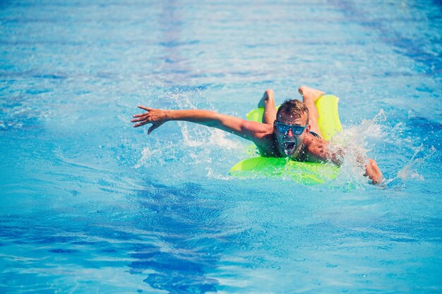 Hübscher junger Mann schwimmt auf aufblasbarer Matratze im blauen Pool