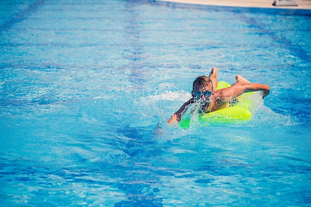 Hübscher junger Mann schwimmt auf aufblasbarer Matratze im blauen Pool