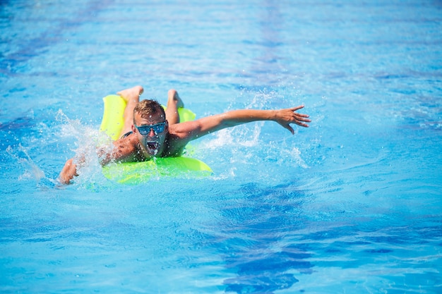 Hübscher junger Mann schwimmt auf aufblasbarer Matratze im blauen Pool