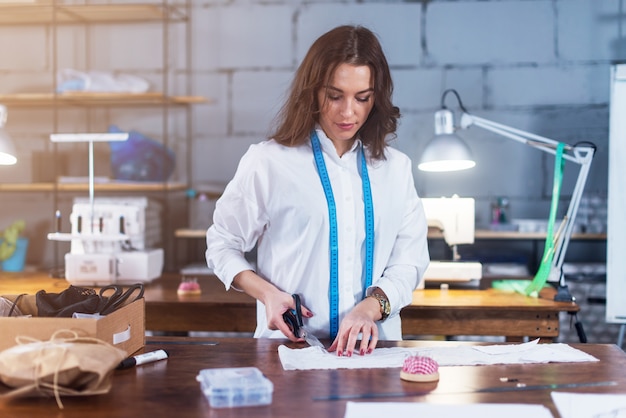 Hübscher junger Modedesigner, der Stoff mit einer Schere während der Arbeit schneidet