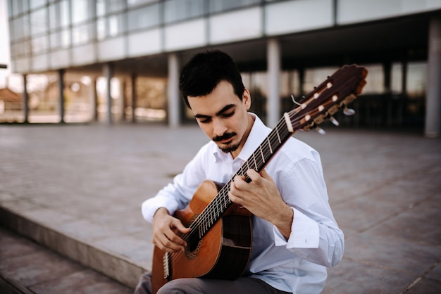 Hübscher junger Musiker, der klassische Gitarre in der Stadt spielt.