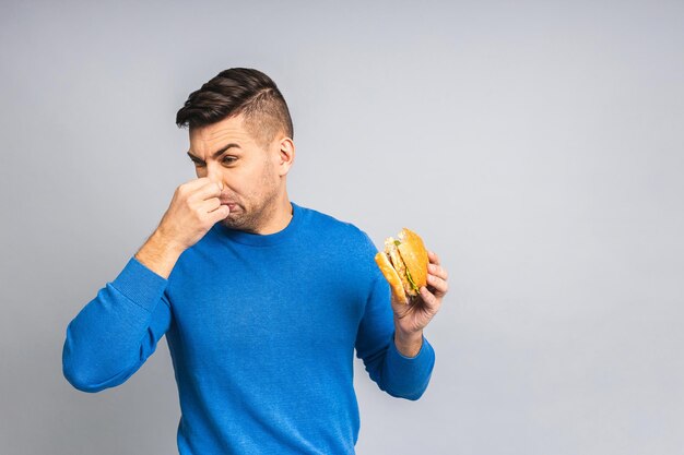 Hübscher junger ukrainischer Mann, der ungesunde Burger ablehnt, die über weißem grauem Hintergrund isoliert sind Diätkonzept mit Kopierraum für Text