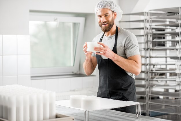 Hübscher Käser in Uniform, der auf dem kleinen produzierenden Bauernhof Käse zu Formen formt