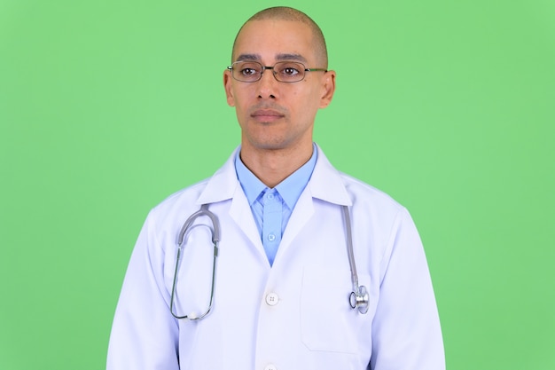 hübscher kahler multiethnischer Mannarzt gegen grüne Wand